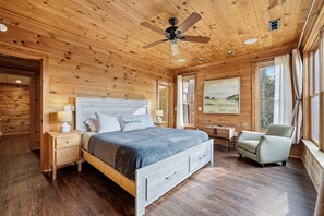 A wooden cabin bedroom with a bed, bedside tables, a chair, and a ceiling fan.