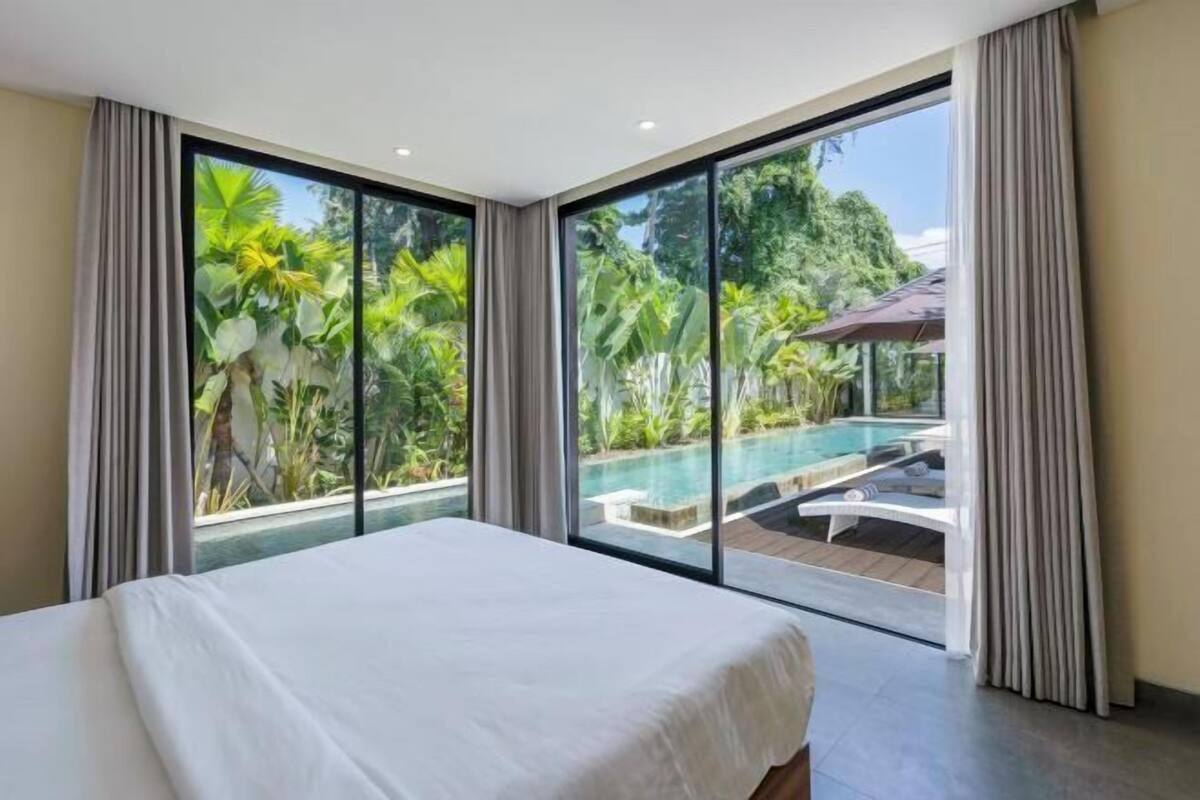 A bedroom with a large bed, a view of a swimming pool, and a balcony with curtains.