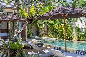 Ein Poolbereich mit Liegestühlen und Sonnenschirmen, umgeben von üppiger Vegetation.