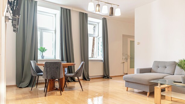 A modern living room with a sofa, a glass coffee table, and a dining area with chairs and a table. - Basic 2BR Apt Near Westbahnhof (Vienna)