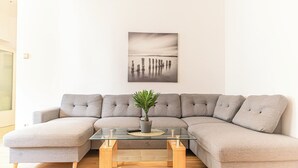 A modern living room with a grey sectional sofa, a glass coffee table with a plant, and a framed photograph on the wall. - Basic 2BR Apt Near Westbahnhof (Vienna)