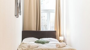 A neatly made bed with a beige quilt, a green pillow, and two rolled towels. - Basic 2BR Apt Near Westbahnhof (Vienna)