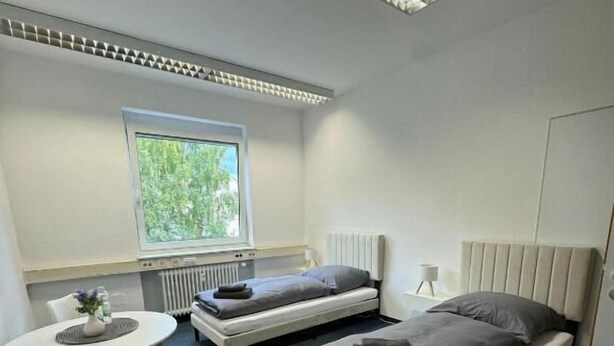 A small, modern room with two beds, a round table, and a chair. - StayFlex Nürnberg (Nuremberg)