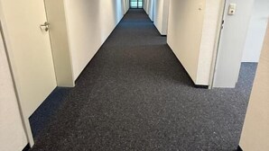 A long, narrow hallway with white walls and a dark carpet. - StayFlex Nürnberg (Nuremberg)