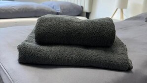 A neatly made bed with a grey duvet and pillows, a white radiator, and a small table with a lamp in a modern room. - StayFlex Nürnberg (Nuremberg)
