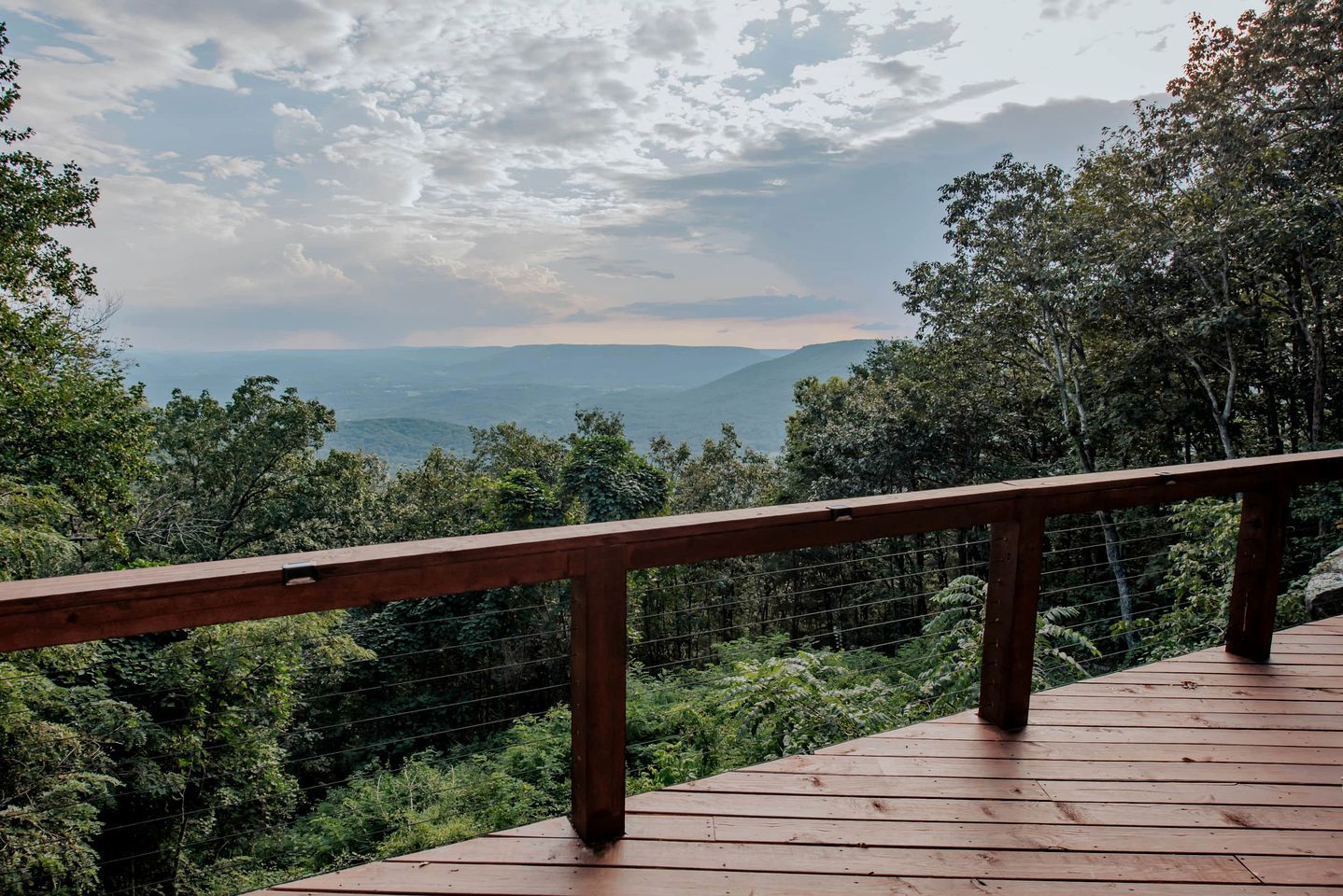 A wooden deck with a metal railing overlooking a mountainous landscape.