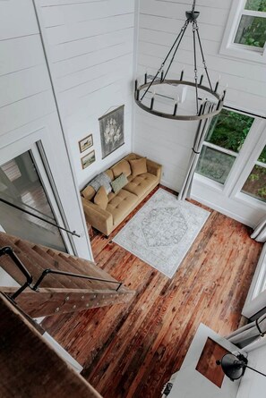 A loft-style room with a wooden floor, a beige sofa, a chandelier, and large windows.