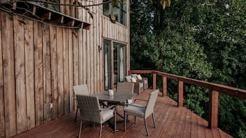 A wooden deck with a table and chairs, a glass door, and a view of a forested area.