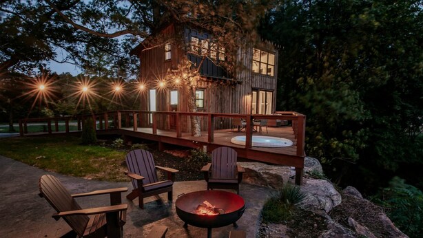 Une cabane en bois dotée d’une terrasse, de meubles de jardin et d’un foyer extérieur.