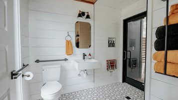Un baño moderno con inodoro, lavamanos, espejo, toallero y baldosas de suelo estampadas.