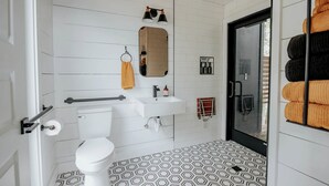 Une salle de bain moderne équipée de toilettes, d’un lavabo, d’un miroir, d’un porte-serviettes et de carreaux de sol à motifs.