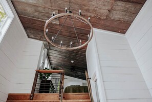 A staircase with a wooden handrail, a circular ceiling light fixture, and a view of a room with a white wall and a window.