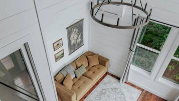 Une pièce de style loft avec un plancher en bois, un canapé beige, un lustre et de grandes fenêtres.