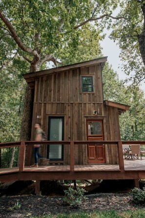 A wooden cabin with a deck, a large window, and a door.