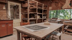 Un atelier rustique, doté de meubles en bois, d’une table à dessin et d’étagères remplies d’outils et de matériaux.