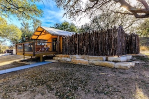 A wooden cabin with a deck and a covered porch, surrounded by a natural landscape.