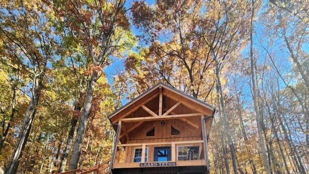 A wooden cabin with a covered porch, surrounded by trees and a wooden deck. - Gorgeous Cabin Great for Family Getaways by Tappan Lake in Ohio (Deersville)