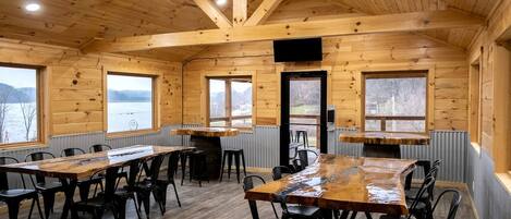 A wooden cabin with a dining area, large windows, and a view of a lake.