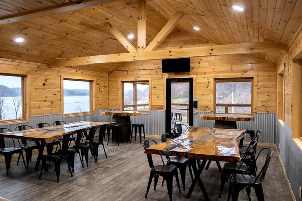 A wooden cabin with a dining area, large windows, and a view of a lake.