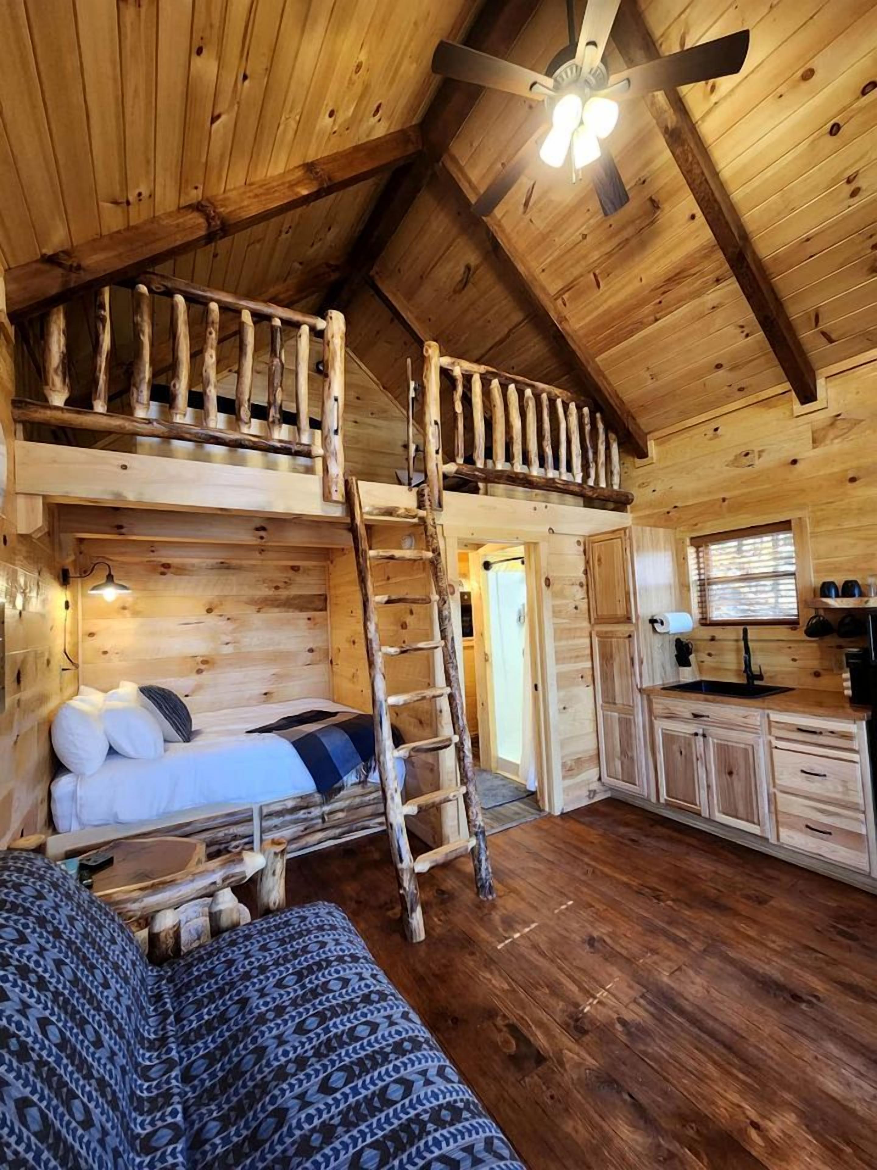 Uma cabana com quarto no mezanino, escada para a cama superior, área de cozinha e ventilador de teto.
