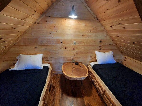 Un cuarto ático pequeño y acogedor con dos camas, una mesa de madera en el centro y una lámpara colgante.