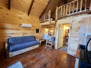 Interior de una cabaña de madera con sofá, una escalera y una zona de cocina.