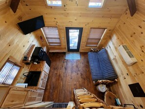 A compact wooden cabin with a kitchenette, a sofa, and a windowed door.