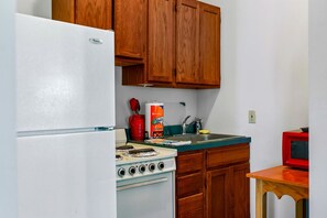 Una cocina con armarios de madera, un refrigerador blanco, una estufa y un televisor rojo.