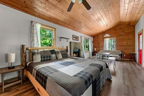 A cozy bedroom with a wooden ceiling, a bed with a quilt, a fireplace, and a dining area.