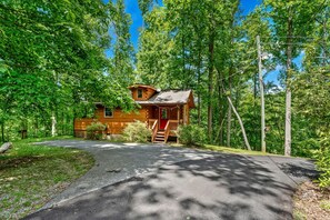 A cabin with a porch, surrounded by trees, and a paved driveway leading to it. - Charming Cabin with Spa and Mountain Views in Sevierville, Tennessee (Sevierville)