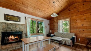 A cozy cabin interior with a stone fireplace, wooden walls, a sofa, and a dining table. - Charming Cabin with Spa and Mountain Views in Sevierville, Tennessee (Sevierville)