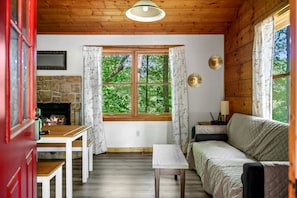 A cozy cabin interior with a stone fireplace, wooden walls, a sofa, a table, and a window with curtains. - Charming Cabin with Spa and Mountain Views in Sevierville, Tennessee (Sevierville)