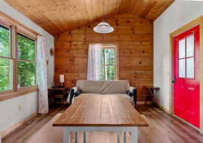 Eine Holzhütte mit rustikalem Interieur, einem Esstisch, einer Couch und einer roten Tür.