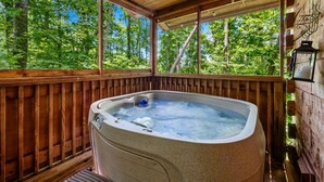 A hot tub in a wooden deck with a view of a forest.