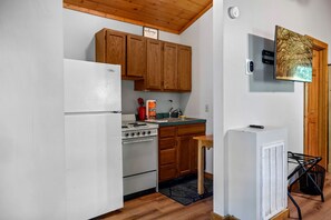Una cocina con alacenas de madera, un refrigerador blanco, una estufa y una pequeña mesa con una silla.