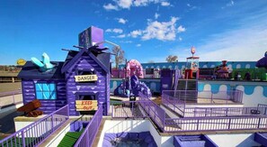 A purple-themed amusement park ride with a 'DANGER' sign, a 'KEEP OUT' sign, and a small building with a flag.