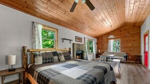 A cozy bedroom with a wooden ceiling, a bed with a quilt, a fireplace, and a dining area.