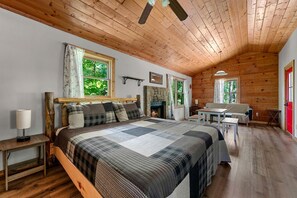 A cozy bedroom with a wooden ceiling, a bed with a quilt, a fireplace, and a dining area.