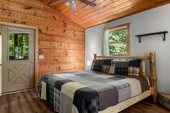 Un dormitorio tipo cabaña de madera con una cama, una ventana y una puerta.