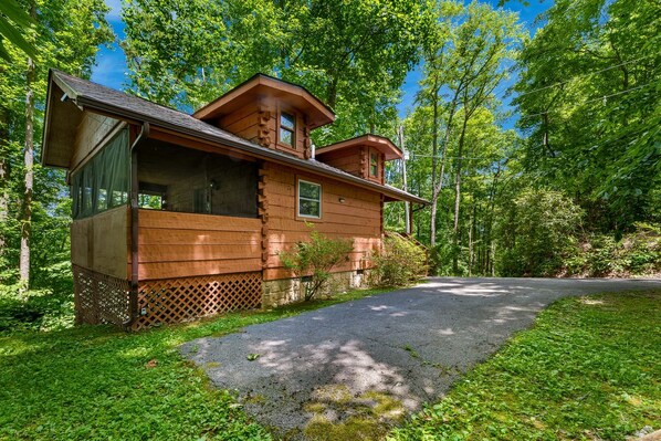 Un chalet rustique doté d’une véranda, entouré d’une végétation luxuriante et surplombant un ciel dégagé.