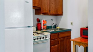 A kitchen with wooden cabinets, a white refrigerator, a stove, and a red television. - Charming Cabin with Spa and Mountain Views in Sevierville, Tennessee (Sevierville)