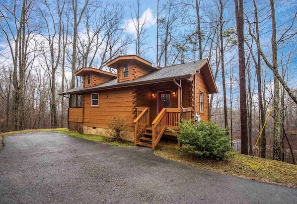 A wooden cabin with a porch, a staircase, and a driveway.