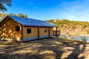 A single-story cabin with a metal roof, a porch, and a view of a lake and trees.