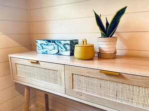 A wooden console table with a woven front panel, a yellow container, and a potted plant. - Luxury Tented Cabin Glamping Escape, with River Access in Ingram, Texas (Hunt)