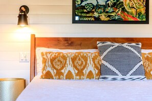 A bed with patterned pillows, a wall-mounted lamp, and a painting.