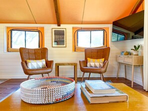 A cozy room with two leather chairs, a woven rug, and a bookshelf. - Luxury Tented Cabin Glamping Escape, with River Access in Ingram, Texas (Hunt)
