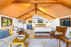 A cozy, well-lit attic bedroom with a bed, seating area, and kitchenette.