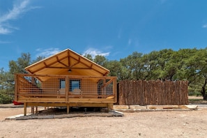 A wooden cabin with a balcony, a fenced area, and a clear sky.