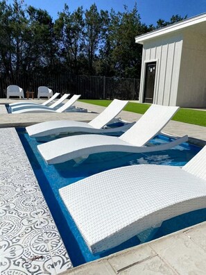 A swimming pool with white lounge chairs and a patterned tile border.