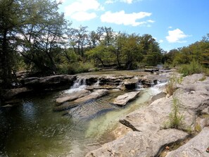 A natural landscape with a clear stream, rocky terrain, and trees. - Luxury Tented Cabin Glamping Escape, with River Access in Ingram, Texas (Hunt)
